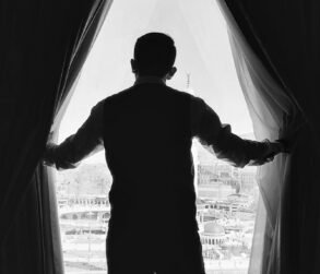 Photo by Eismayeel Zain A man in silhouette looks out a window towards Mecca, capturing a serene urban landscape.